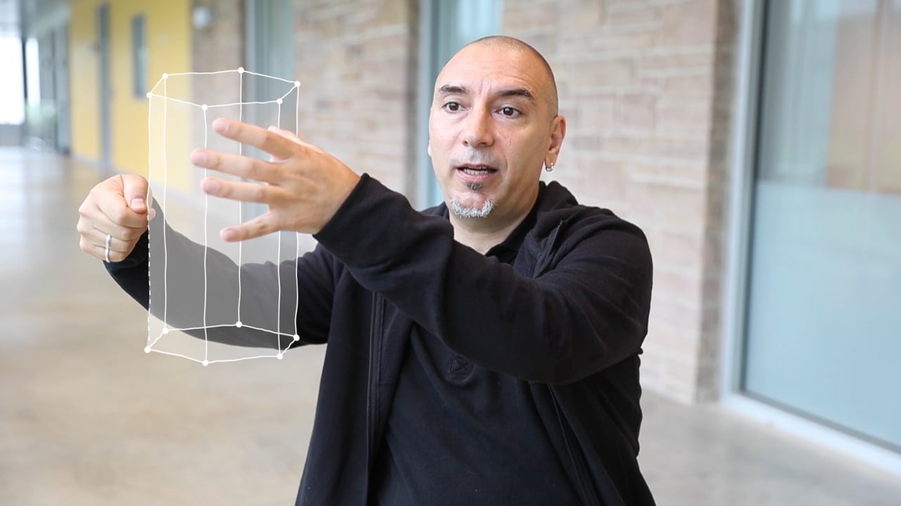 Presenter gesturing toward a wireframe prism in a scutoid explainer video still